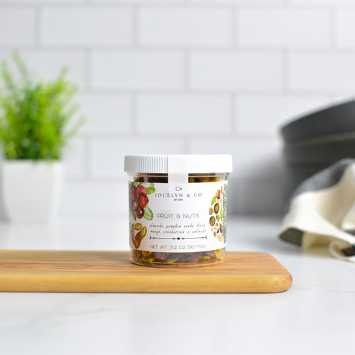 Jar of 'Fruit & Nuts' on a wooden cutting board with a white tiled wall background