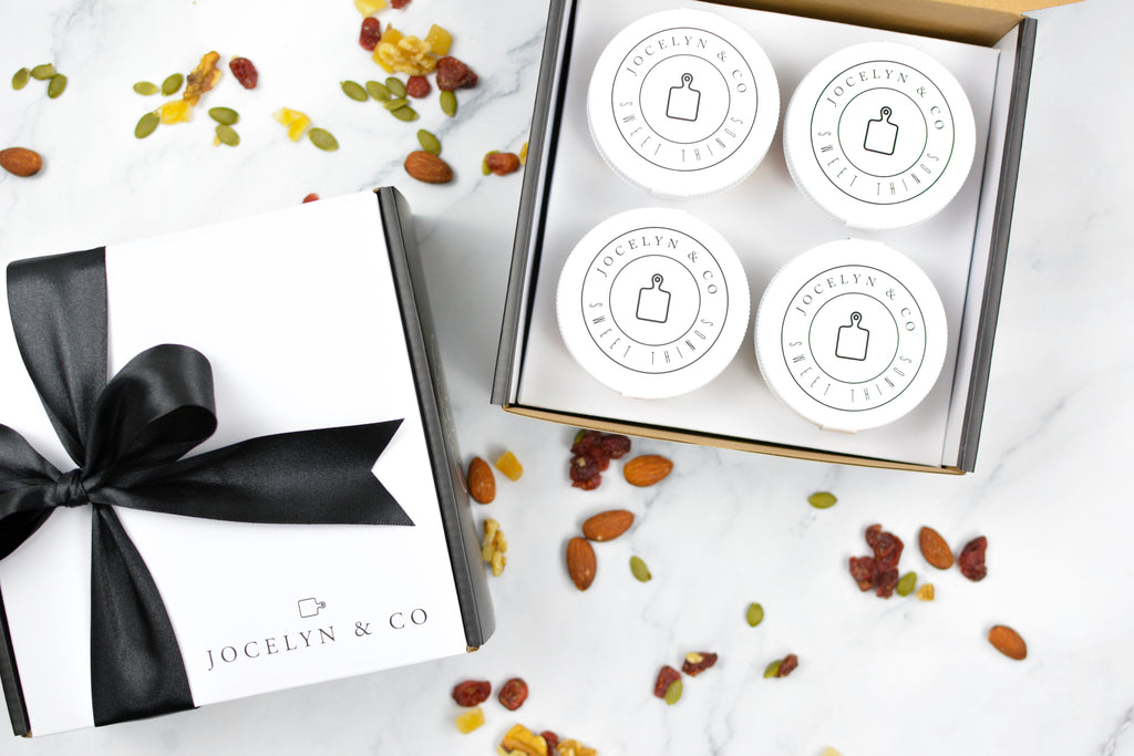 Four round white containers with black text on a white surface with a black ribbon and decorative stones.