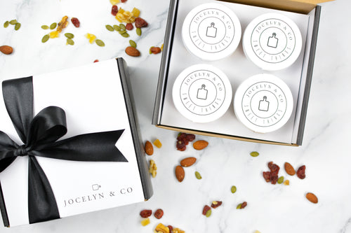 Four round white containers with black text on a white surface with a black ribbon and decorative stones.