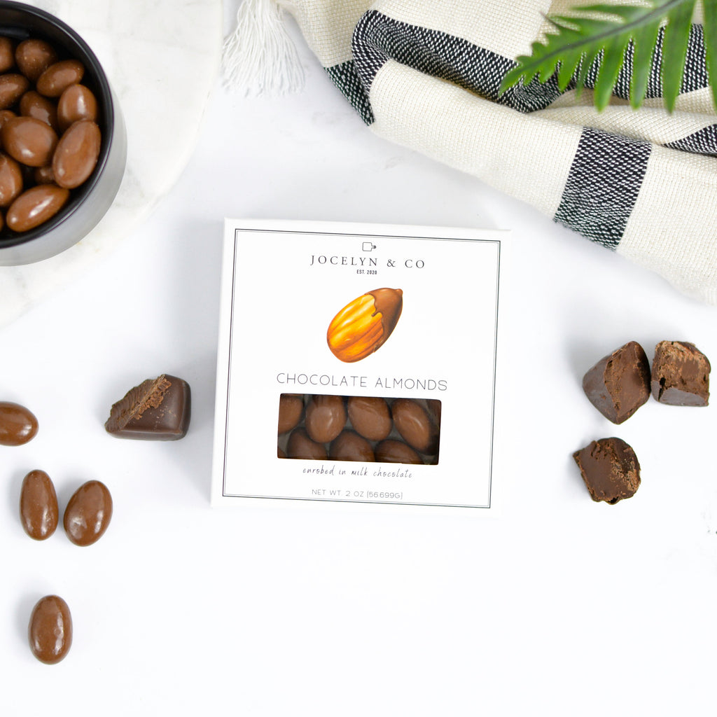 Chocolate almonds on a marble surface with a box and a plant in the background