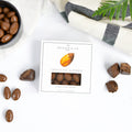 Chocolate almonds on a marble surface with a box and a plant in the background