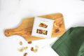 Jocelyn & Co. Mixed Nuts box on a wooden serving board with loose cashews, almonds and pecans