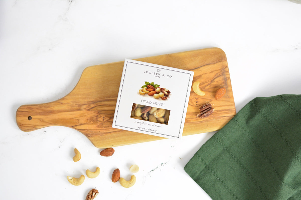 Jocelyn & Co. Mixed Nuts box on a wooden serving board with loose cashews, almonds and pecans